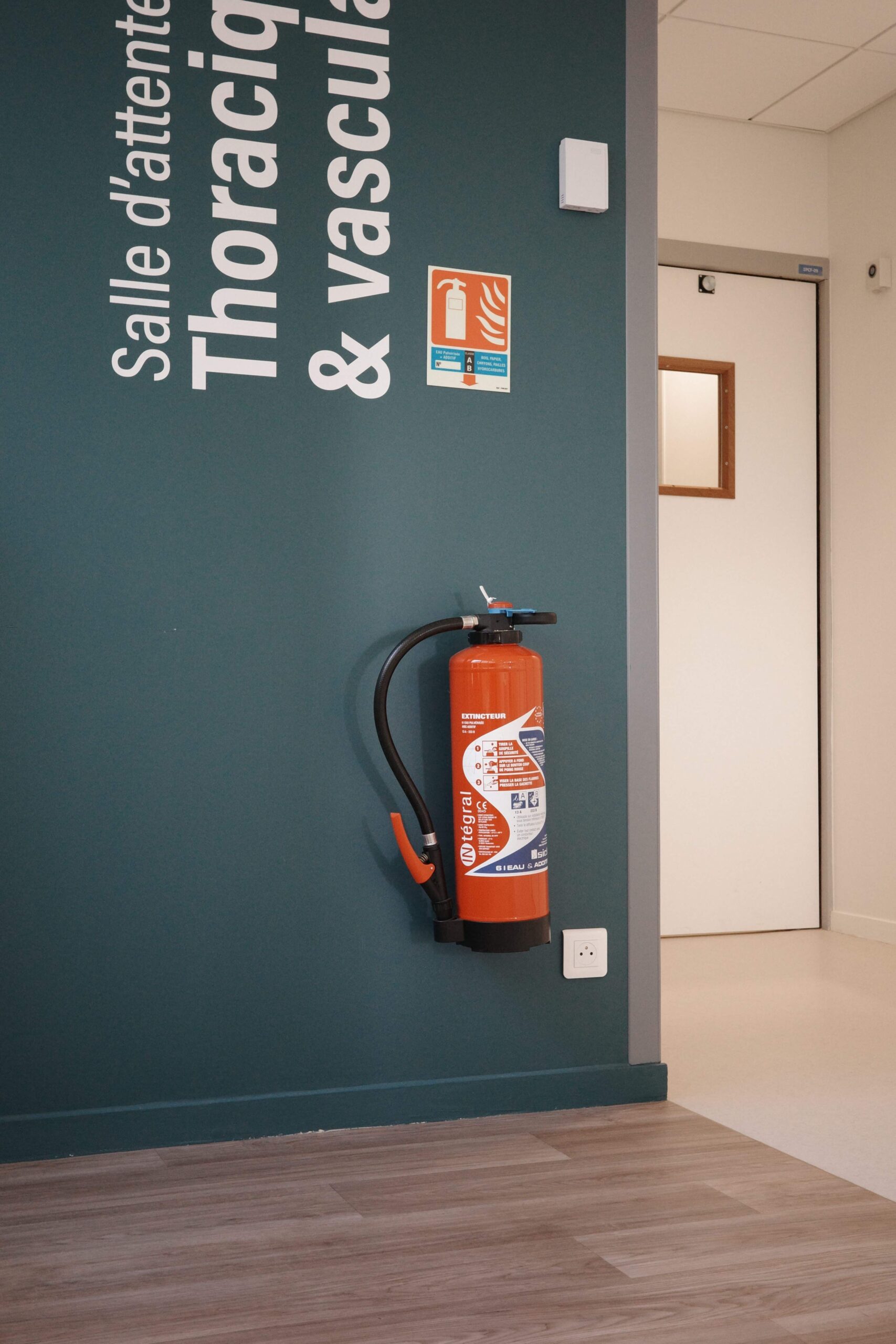 Extincteur accroché sur un mur gris foncé.
