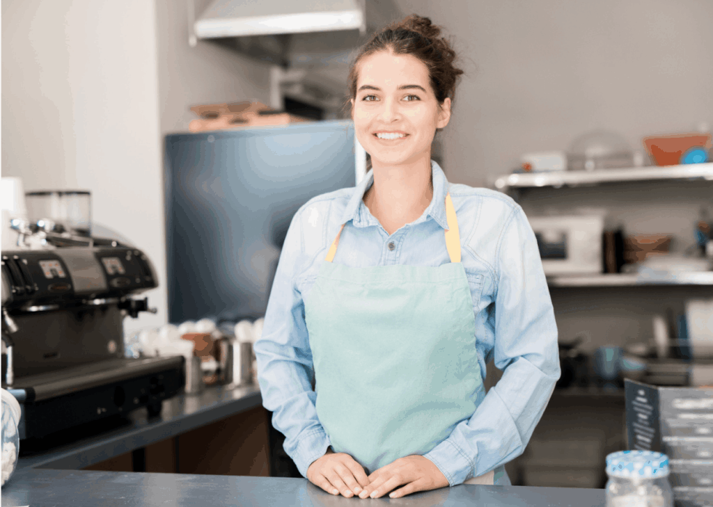 Jeune femme portant un tablier et une chemise, derrière le comptoir d'un café. 