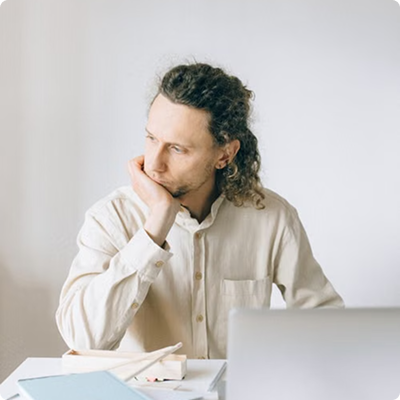 Homme portant une chemise, l'air pensif devant son ordinateur portable.