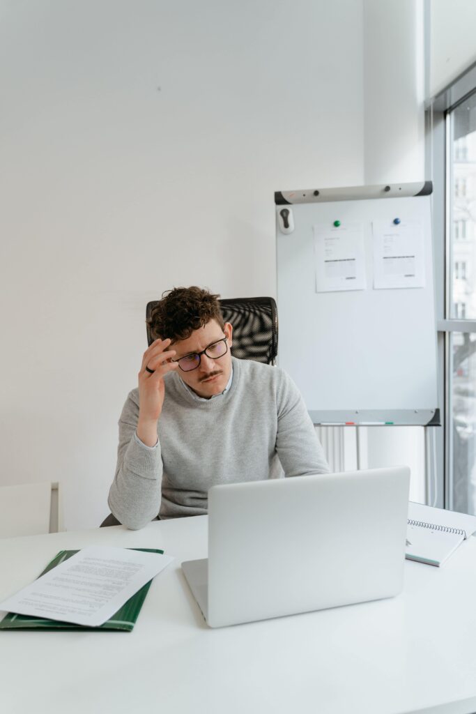 Homme trentenaire, assis à son bureau devant son ordinateur portable.